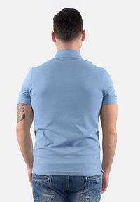 Polo shirt azzurro chiaro a maniche corte con colletto, texture liscia e design aderente. Presenta un fondo spaccato e dettagli di cucitura sottili.