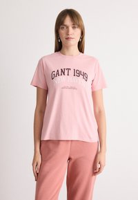 T-shirt di cotone rosa con maniche corte e scollatura rotonda. Presenta la scritta "GANT 1949 NEW HAVEN" stampata in lettere grasse scure sul davanti.