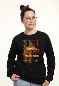 Felpa nera con un grafico di granchio con accenti arancioni e gialli, testo che riporta "OCEAN" e "NORTH PACIFIC," e una vestibilità rilassata.