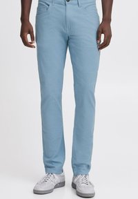 Lichtblauwe chino's van katoen. Slim fit ontwerp met vier zakken. Knop- en ritssluiting, gladde textuur, gecombineerd met grijze sneakers.