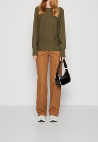 Olive green ribbed sweater, tan wide-leg pants, and white sneakers. Black glossy handbag with a shoulder strap. Simple and casual outfit.