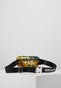 Belt bag con stampa floreale gialla, chiusura a zip e tracolla nera regolabile con logo "VERSACE". Realizzato in materiale sintetico.