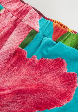Tela multicolor con grandes patrones florales rojos, con secciones en tonos teal y verde. Textura suave con un detalle de cintura elástica fruncida.