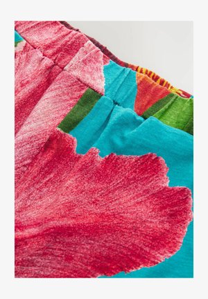 Tela multicolor con grandes patrones florales rojos, con secciones en tonos teal y verde. Textura suave con un detalle de cintura elástica fruncida.