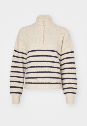Beige trui met marineblauwe horizontale strepen, hoge kraag en een half-rits sluiting. Gemaakt van een geweven textiel, met geribde mouwen.