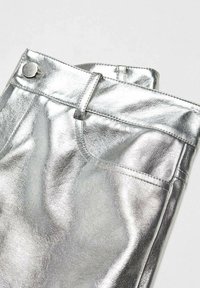 Pantalon en similicuir métallisé argenté à texture lisse, avec une passants pour ceinture et une poche avant, soigneusement plié à la taille.