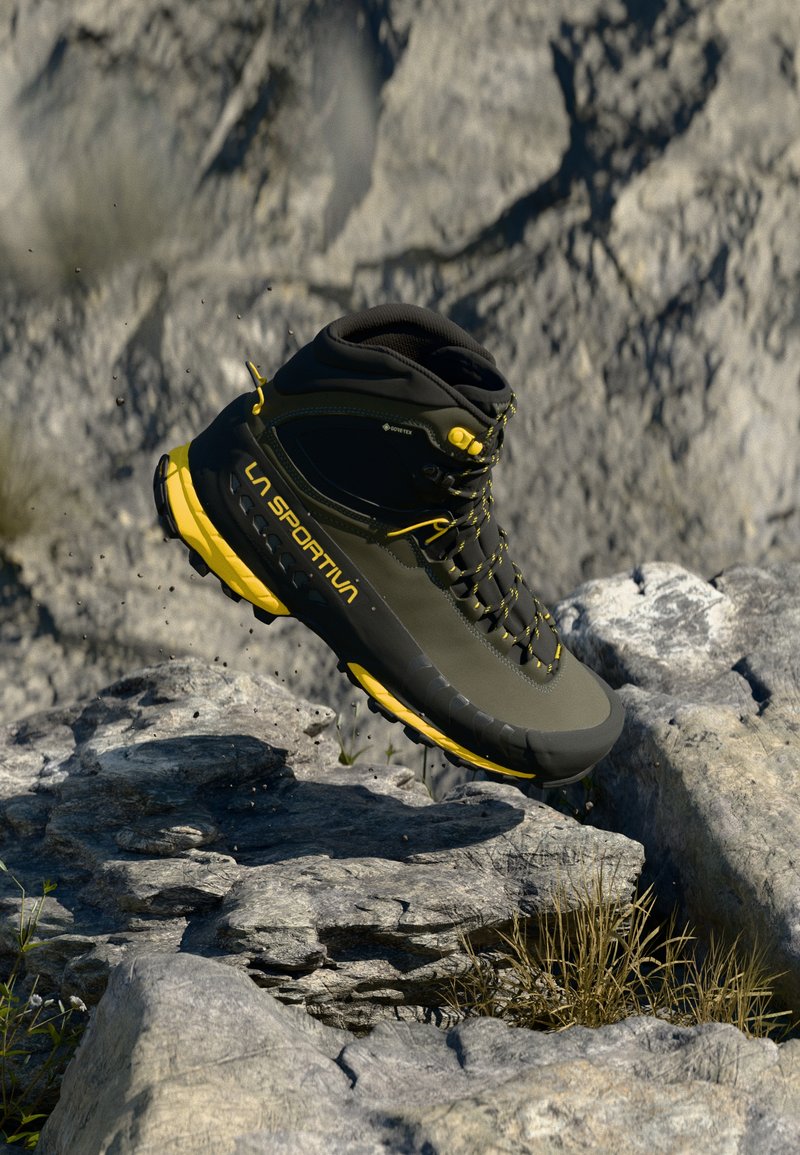 Čierna a žltá turistická obuv La Sportiva pristáva na skalnatom teréne s malými prachovými časticami a suchou trávou okolo.