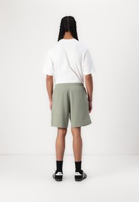 Vit kortärmad t-shirt i kombination med gröna skräddarsydda shorts i en texturerad kvalitet. Bärs tillsammans med svarta strumpor och svarta sneakers.