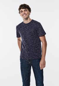 Mörkblå kortärmad skjorta med en strukturerad mönstring, i kombination med mörkblå jeans. Enkel rund halsdesign med minimalistisk branding på bröstet.