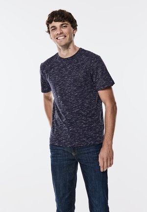 Navy blauwe kortärmshemd met een gestructureerd patroon, gecombineerd met donkere blauwe jeans. Eenvoudig ronde hals ontwerp met minimalistische branding op de borst.