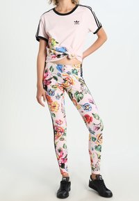 Rosa kortärmad t-shirt med blommönster och svarta detaljer, kombinerat med leggings med blommönster och svarta sidostråk samt svarta sneakers.