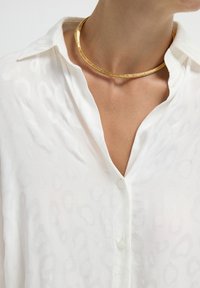 White, semi-sheer button-up shirt with a subtle leopard pattern. Gold choker necklace around the neck, smooth texture.