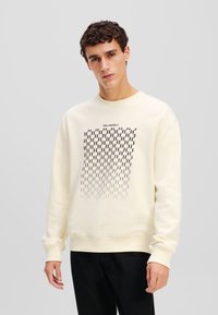 Crèmekleurige sweatshirt met ronde hals en lange mouwen. Heeft een zwart grafisch patroon en de tekst "KARL LAGERFELD" erboven.