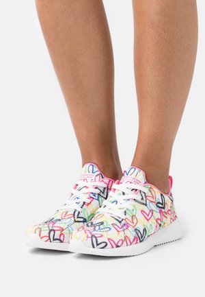 Flerfärgad sneaker med hjärtmönster, gjord av lätt tyg. Har vita snören och gummisula, med rosa detaljer på kragen.