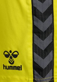 Helle gelbe Sportshorts mit einem schwarzen Chevron-Musterstreifen. Enthält ein schwarzes Logo in der unteren linken Ecke. Weicher, leichter Stoff.