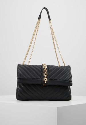 Czarna pikowana skórzana torebka na złotym łańcuszku z centralnym zapięciem, prezentowana na białej powierzchni na neutralnym tle.