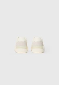 White athletic sneakers featuring a smooth, textured upper and a translucent heel cushioning detail. Suede accents provide contrast.