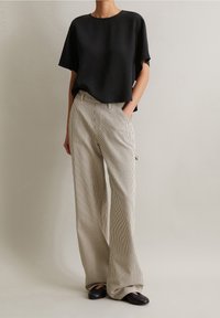 Top corto nero a maniche corte con una vestibilità comoda abbinato a pantaloni ampi a righe beige e bianche. Tessuto liscio con una lucentezza sottile.