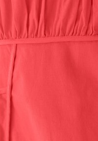 Tessuto color corallo con una texture morbida, caratterizzato da dettagli arricciati nella parte superiore e una finitura liscia lungo le cuciture.