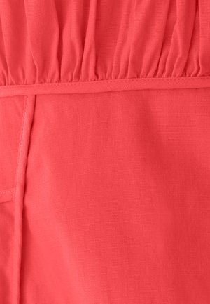 Tessuto color corallo con una texture morbida, caratterizzato da dettagli arricciati nella parte superiore e una finitura liscia lungo le cuciture.