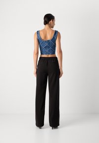 Top de mezclilla azul recortado con un diseño acolchado, combinado con pantalones negros de cintura alta. Los pantalones cuentan con una cinturilla elástica y bolsillos laterales.