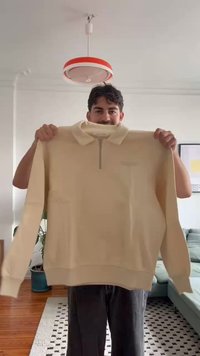 Sudadera de color beige claro con media cremallera, mangas largas, puños y dobladillo acanalados, y un pequeño logo en el pecho. Textura suave.