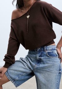 Pull marron à épaules dénudées avec poignets côtelés, associé à un short en denim bleu clair coupe ample présentant un motif délavé et des poches avant.