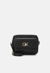 Černá kožená crossbody taška se zlatým logem, obdélníkový tvar, klopový uzávěr, nastavitelný popruh, hladká textura a minimalistický design.