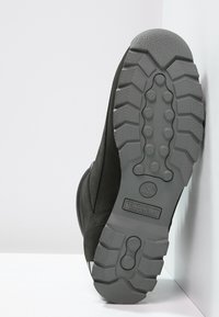 Bota Timberland negra, con una suela de goma resistente que presenta patrones de tracción profundos y una parte superior texturizada. Logo grabado en la suela exterior.