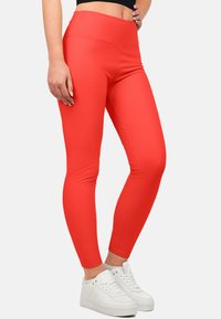 Rode leggings van rekbaar materiaal met een gladde afwerking, voorzien van een hoge tailleband en een aansluitend ontwerp, gecombineerd met witte sneakers.