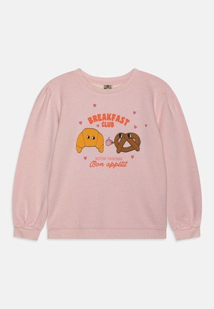 Sweat-shirt rose à manches longues avec un croissant et un bretzel dessinés tenant une tasse de café, entourés de cœurs, texte "Breakfast Club" et "Bon appétit".