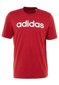 Červené krátké tričko Adidas s bílým výrazným logem "adidas" uprostřed na hrudi, kulatým výstřihem a pravidelným střihem.