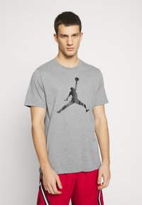Camiseta de algodón gris con una silueta negra de un jugador de baloncesto. Manga corta y cuello redondo, combinada con pantalones cortos rojos.