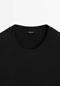 Schwarzes Rundhals-T-Shirt aus Baumwolle. Es hat eine glatte Textur und ein einfaches Design mit einem Etikett, auf dem "Massimo Dutti, Hergestellt in Kambodscha" steht.
