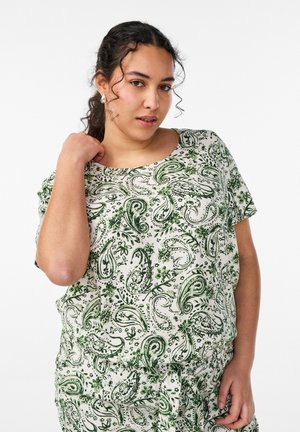 Donna con capelli scuri, indossa una maglia morbida a maniche corte e pantaloni abbinati con motivo paisley verde e floreale.