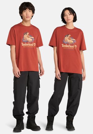 Rustrøde bomulds t-shirts med grafisk print, parret med sorte cargo bukser og sorte snørebogs støvler. Casual fit, korte ærmer.