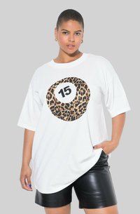 Hvid oversized t-shirt med en rund leopardprint grafik og nummeret "15" i sort i midten. Modellen har sorte faux læder shorts på.