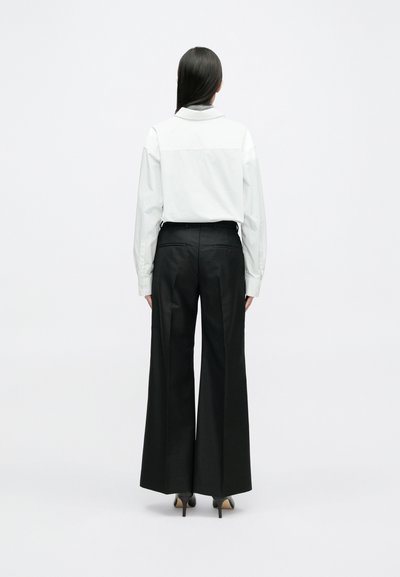 Λευκό πουκάμισο με γιακά, σε συνδυασμό με παντελόνι μαύρο ψηλόμεσο. Το παντελ�όνι είναι φαρδύ και έχει λεία υφή.