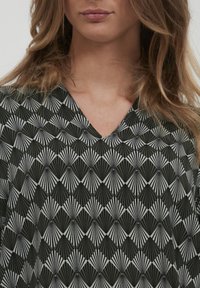 Top a motivi in bianco e nero con scollo a V, caratterizzato da forme a ventaglio alternati e dettagli testurizzati.