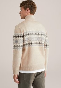 Beżowy sweter dziany z wysokim kołnierzem, z wzorzystym pasem w jasnoniebieskim i czarnym kolorze na plecach. Ściągacze przy mankietach i u dołu.