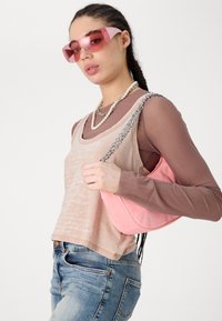 Borsa in suede rosa con catena, canottiere sovrapposte in beige e marrone, occhiali da sole rosa e collana di perle. Jeans in denim casual.