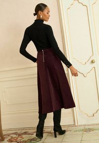 Dolcevita nero a coste e lunga gonna bordeaux con cerniera posteriore, abbinati a stivali neri con tacco al ginocchio. Texture liscia e design aderente.