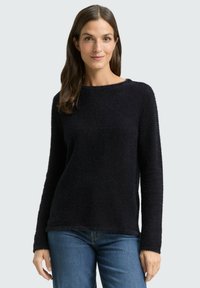 Black, textured pullover sweater with long sleeves and a round neckline, paired with blue denim jeans. Informal and cozy fit.