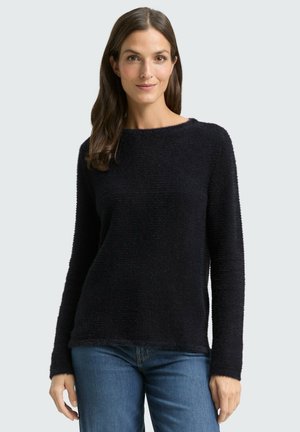 Black, textured pullover sweater with long sleeves and a round neckline, paired with blue denim jeans. Informal and cozy fit.