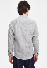 Camicia a maniche lunghe grigia a fantasia con colletto a scatto, polsini regolabili e orlo curvo, caratterizzata da un tessuto leggermente strutturato.