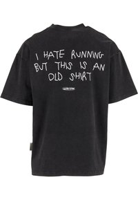 Černé oversized tričko s bílým ručně psaným textem "Nesnáším běhání, ale tohlecto je staré tričko" a malým logem "Another Cotton" dole.