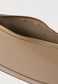 Beige bőr tasak arany cipzárral, félig nyitva, amely puha velúrra hasonlító belső bélést mutat.