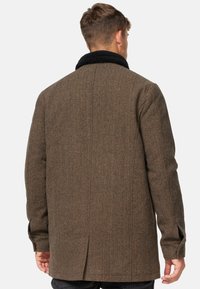 Brun uldblandingsfrakke med en sort sherpa-krave, struktureret form og sideslids. Har knapper ved håndleddene og en tekstureret overflade.