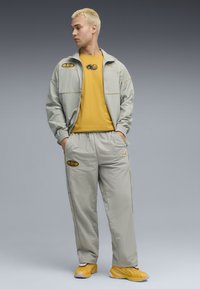 Lys grå vindjakke med elastiske manchetter, gule detaljer og mærker, parret med lys grå bukser og gule sneakers.