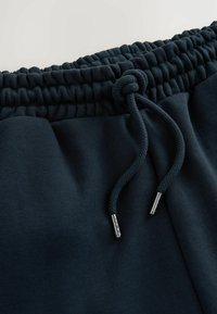 Mørkeblå sweatpants med en struktureret elastisk talje og snor. Snoren har metalagtige ender for holdbarhed.